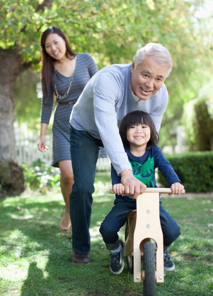 grandfather teaching child to ride bike while mother watches in the background